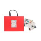 Red gift bag with black handles and various colorful sticker sheets beside it.