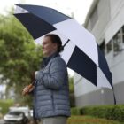 Woman in a gray jacket holding a large black and white umbrella on a rainy day.
