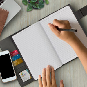 A person writing on a black, custom-branded diary