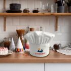 Chef hat on a kitchen counter with shelves, kitchenware, and colorful party hats.
