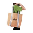 Person holding a large tan tote bag with gray handles and a logo.