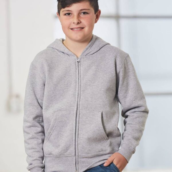 Boy in gray hoodie and jeans smiling, standing indoors.