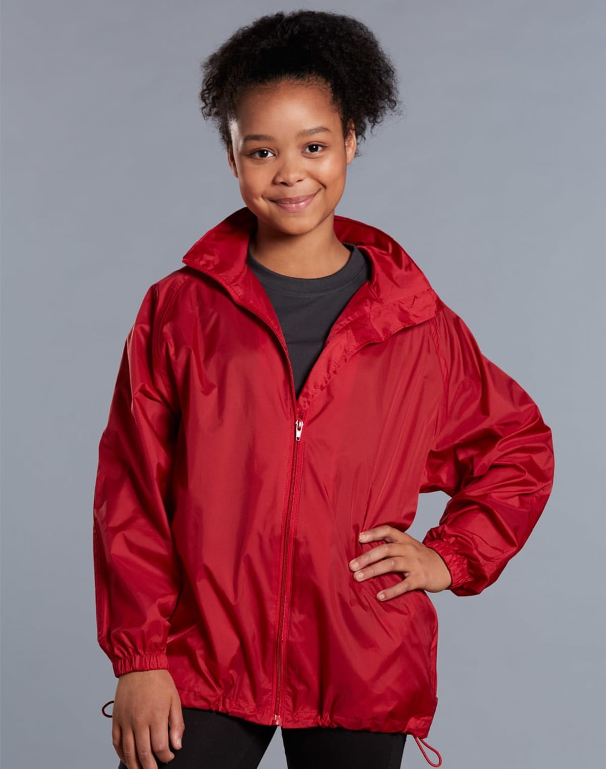 Person smiling, wearing a red zip-up jacket with a neutral gray background.