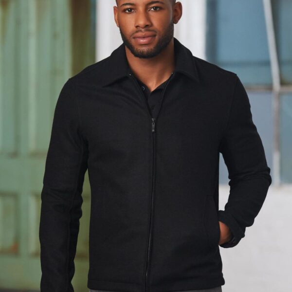 Man in black jacket with short hair stands indoors, hand in pocket, looking at the camera.