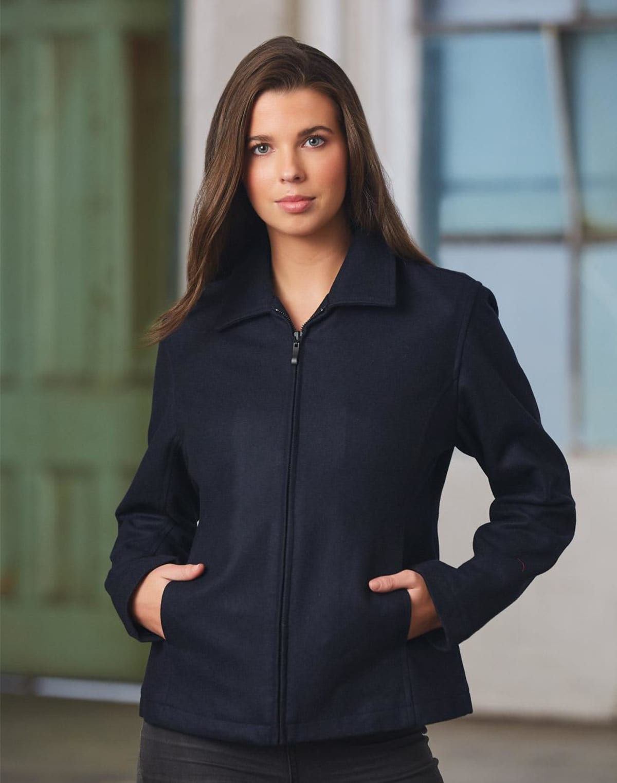 Person wearing a dark jacket with hands in pockets, standing indoors.