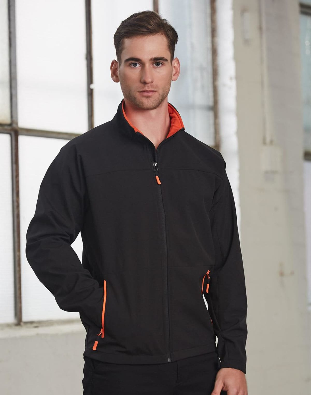 Man in black jacket standing in front of large windows indoors.