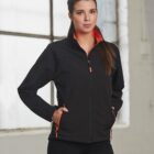 Woman in black jacket with orange trim stands in front of window.