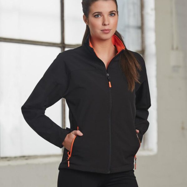 Woman in black jacket with orange trim stands in front of window.
