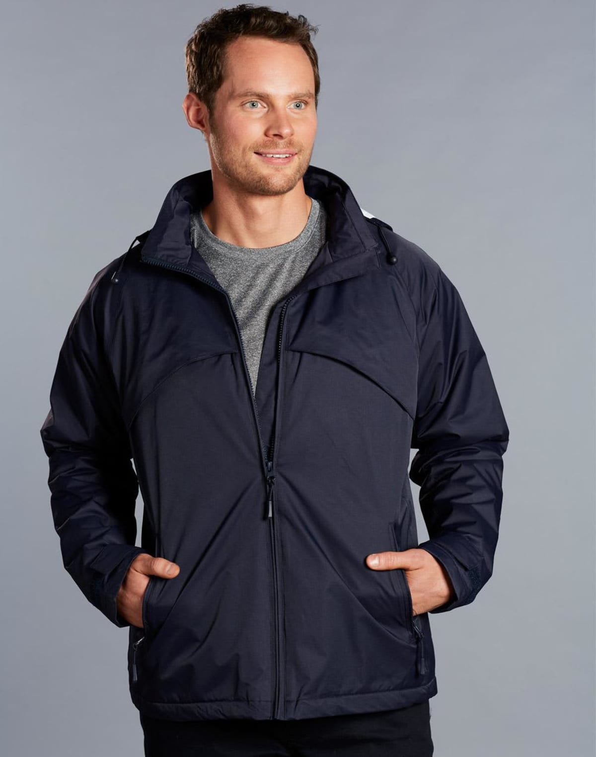 Man wearing a navy jacket and gray shirt, smiling against a gray background.