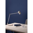 Minimalist desk with a white lamp, two notebooks, a pen, and a glass of water.