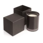Black candle in a glass jar next to an open and closed black square box on a white background.