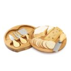 Round wooden cheese board with crackers, cheese, and three cheese knives in a separate tray.