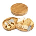 Round bamboo cheese board set with cheese, crackers, and three cheese knives in a storage tray.
