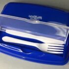 Blue utensil case with a white fork and knife inside under a transparent lid.