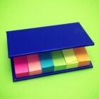 Colorful sticky notes in a blue holder on a bright green background.