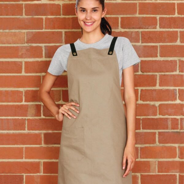 Person in a beige apron and gray shirt standing against a brick wall.