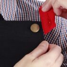 Person attaching a red ribbon to a black apron with gold button, wearing a checkered shirt.