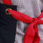 Red apron ties against a checkered shirt and black fabric, with a metal eyelet detail.