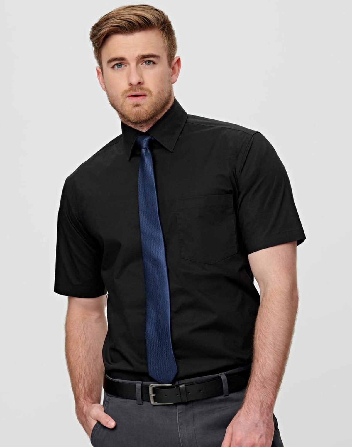 m7020s_01 Man in black short-sleeve shirt and blue tie, standing against a plain background.