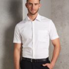 Man in a white short-sleeve shirt and black pants standing against a gray background.