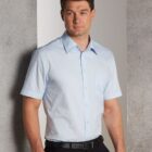 Man wearing a light blue short-sleeve shirt and black pants, standing indoors.