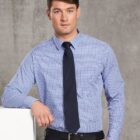 Man in a blue checked shirt and black tie standing against a gray background.