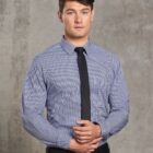 Person in a blue checkered shirt and black tie stands against a concrete wall.