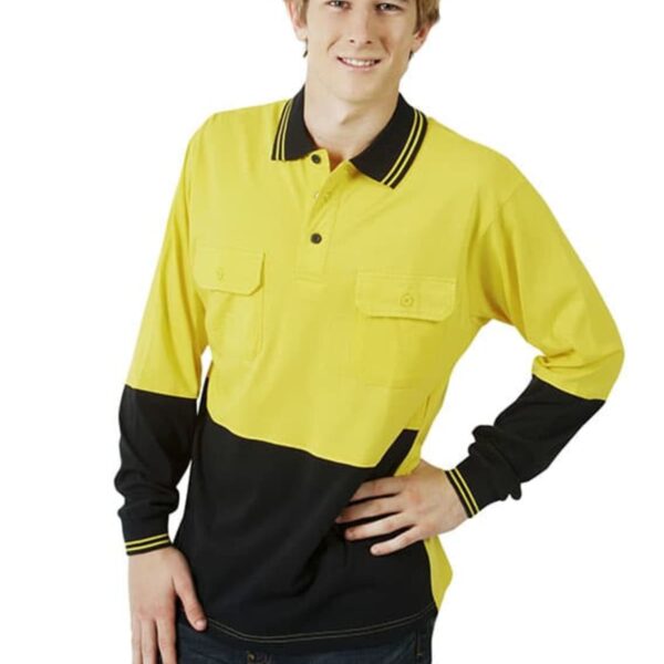 A person wearing a long-sleeve, yellow and black collared shirt with two front pockets poses with one hand on their hip. They have short hair and are smiling. The person is also wearing dark jeans. The background is plain white.