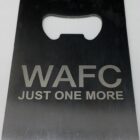 A metal bottle opener with a rectangular shape, featuring a cut-out for opening bottles. The text WAFC JUST ONE MORE is engraved on its surface.