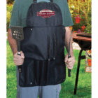 Person wearing an Omaha Steaks apron holding a Promotional BBQ Master Chef Set by a grill outdoors.