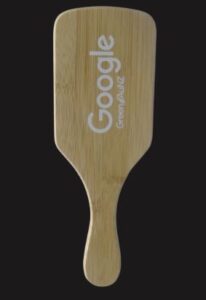Bamboo paddle with Google Green ANZ printed on it, against a black background.