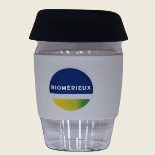 branded mugs glass with black lid, white sleeve, and BioMérieux logo.