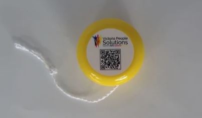 Yellow yo-yo with a QR code and text Victorus People Solutions on a white surface.