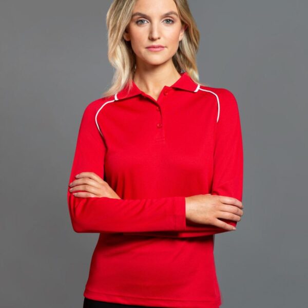 Woman in red long-sleeve polo stands against a gray background, arms crossed.