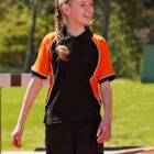 Girl in sportswear smiles on a track field, with trees in the background.