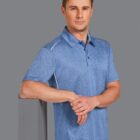 Man in blue polo shirt leaning on a gray surface with arms crossed.