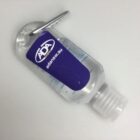 Clear hand sanitizer bottle with a blue ADA label and a silver clip attached.