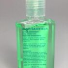 Clear bottle of green hand sanitiser with product information printed on the front label.