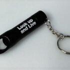 Black keychain bottle opener with Look up and Live text printed on it.