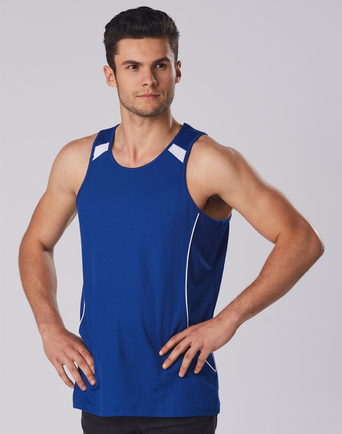 Man in blue athletic tank top with hands on hips against a gray background.