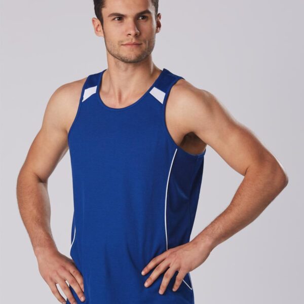 Man in blue tank top standing with hands on hips, looking to the side.