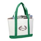 White tote bag with green handles, magazines inside, and a laurel logo on the front pocket.