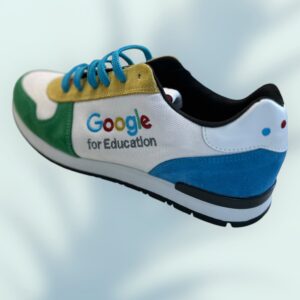 This colorful sneaker doubles as a unique promotional product with Google for Education embroidered on the side. It features green, yellow, blue, and white panels, complemented by a blue lace and black sole on a blurred light blue background.