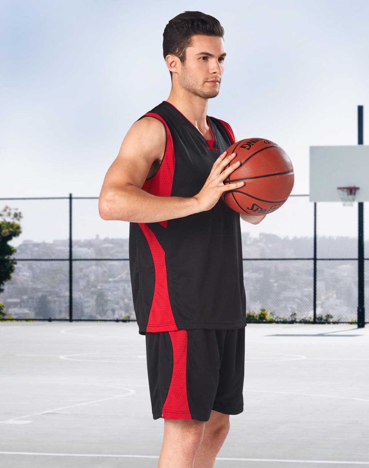 Person in black and red basketball attire holding a ball on an outdoor court.