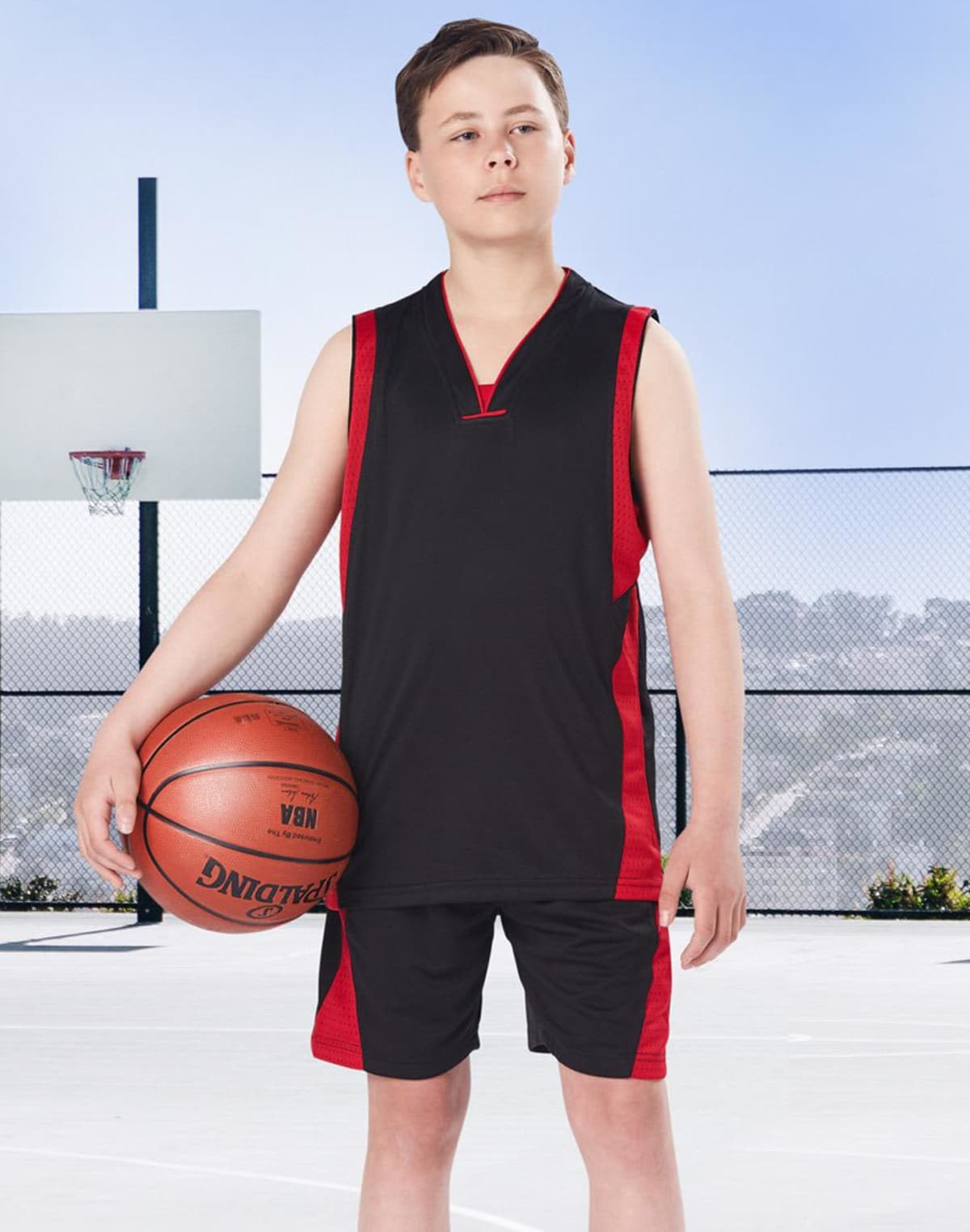 Teen boy in basketball attire holds ball on outdoor court.