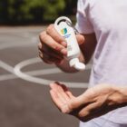 Person applying sunscreen from a small bottle on a basketball court outdoors.