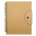 A closed, brown spiral notebook is positioned with its spiral on the left side. A round closure flap with a black dot is on the right. The cover has a plain, matte texture.
