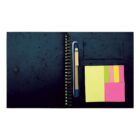 Open black spiral notebook with a blue pen tucked inside. On the right page, there are sticky notes in yellow, pink, and green, alongside a business card holder. The notebook is on a white background.