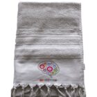 A light gray towel featuring an embroidered design of colorful gears in the shape of a brain and the word BRAINSTORM below it. The towel has a textured top half and fringed tassels along the bottom edge.
