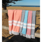 Four colorful striped towels hang on a wooden fence at a sandy beach, ocean in background.